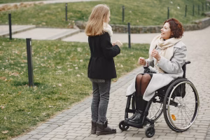 Disabled woman in wheelchair with daughter. Family walking outside at park.