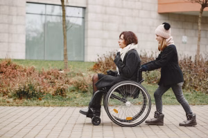 Disabled woman in wheelchair with daughter. Family walking outside at park.